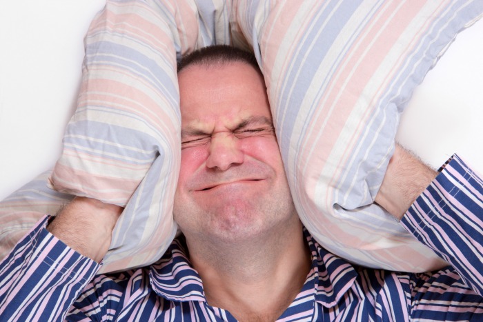 a frustrated tired man hides her head in her pillow