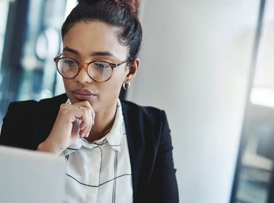 Woman in glasses thinking at her office laptop, weighing a decision