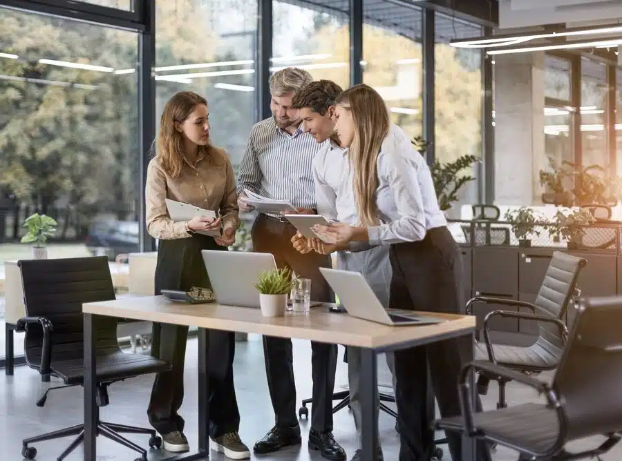 Tech workers collaborating around laptops in a modern office during emotional intelligence training in an AI world